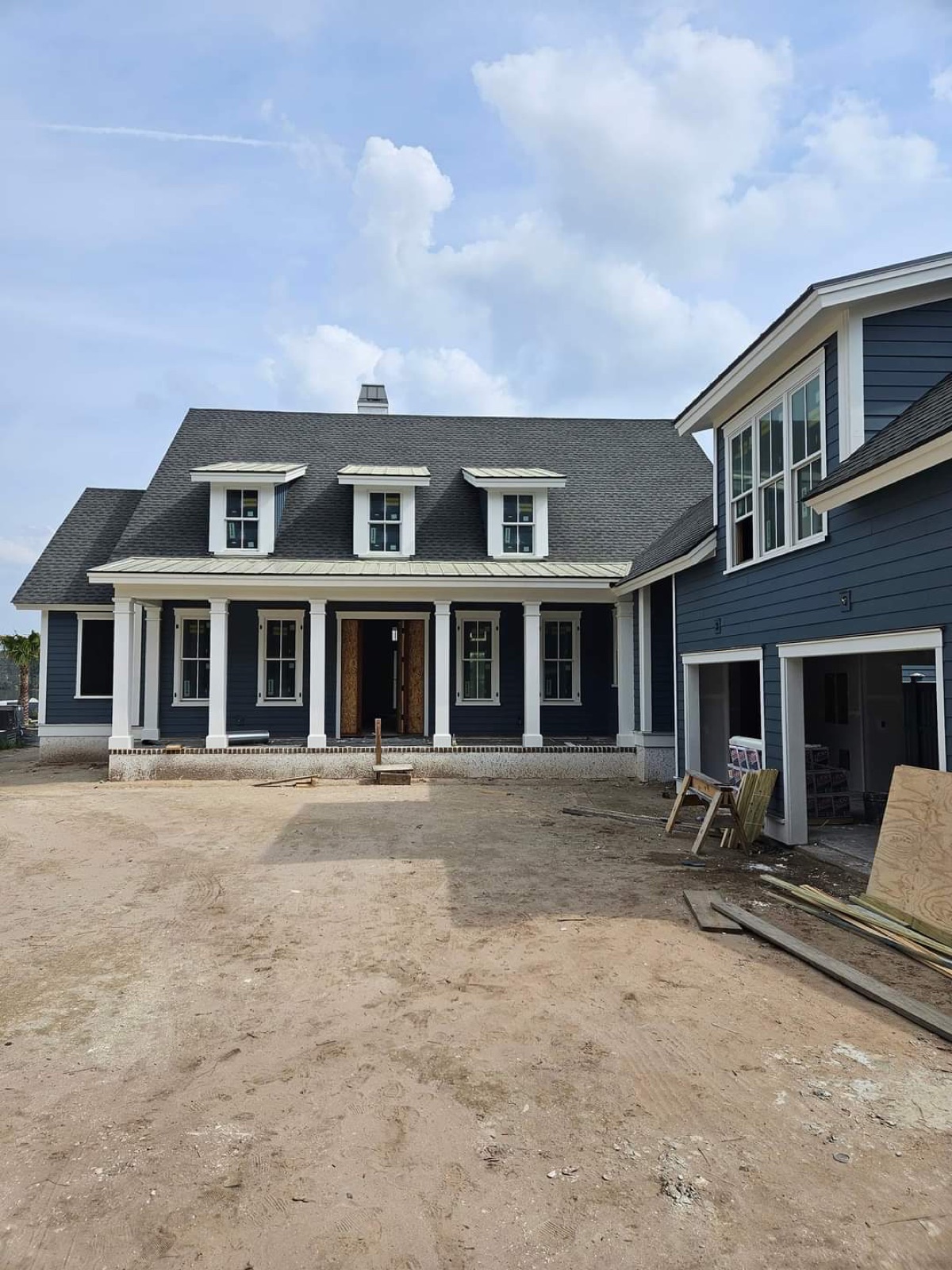 A custom home under construction in the Bluffton, SC area with navy siding, a covered front porch and dormer windows