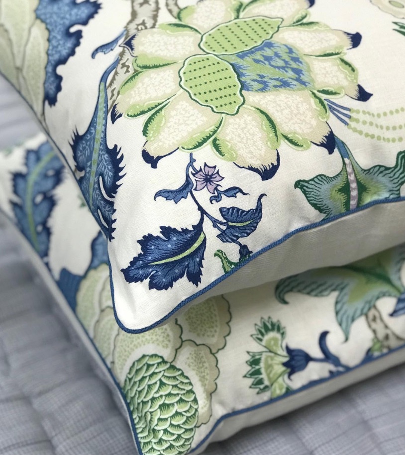 Two stacked pillows in a blue and green floral designer fabric with tailored piping